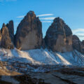 Snow-dusted jagged mountain peaks rise under a clear blue sky in a high alpine landscape.