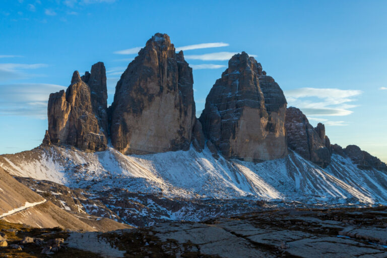 Snow-dusted jagged mountain peaks rise under a clear blue sky in a high alpine landscape.
